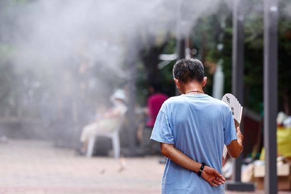 폭염 속 서울역 쪽방촌 인근 한 공원에서 주민이 쿨링포그를 맞으며 부채질을 하고 있다. [사진=연합뉴스]