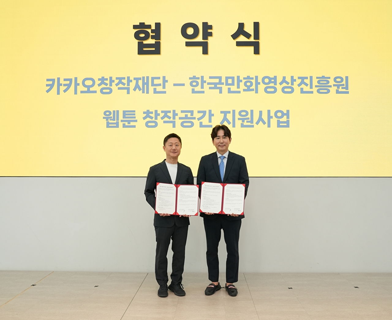 조한규 카카오창작재단 이사장(왼쪽)과 백종훈 한국만화영상진흥원장이 한국만화영상진흥원 클러스터(웹툰융합센터 및 비즈니스센터)에 입주한 웹툰 작가들의 창작 공간 지원 사업 확대를 위한 업무협약 기념 사진을 찍고 있다. [사진=카카오창작재단]