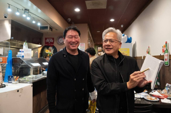 지난 5일(현지시간) 미국 캘리포니아 산타클라라의 한국식 호프집 '99치킨'에서 가진 최태원 SK그룹 회장과의 만찬회동에서 젠슨 황 엔비디아 최고경영자가 신간 '슈퍼모멘텀'을 펼쳐보이고 있다. 2026.2.11 [사진=연합뉴스]