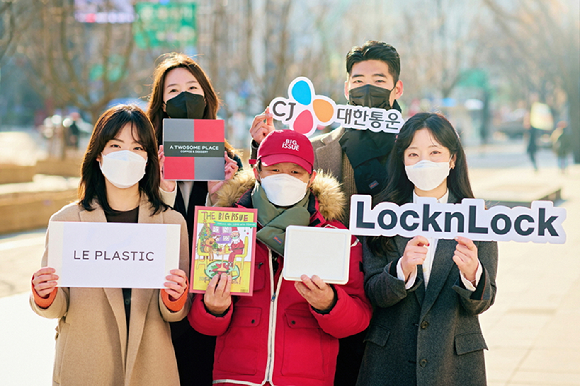 CJ대한통운, 락앤락, 투썸플레이스, K.O.A 직원들이 빅이슈 판매원과 기념 사진을 찍고 있다. 빅이슈 판매원이 폐플라스틱 업사이클링 패딩 목도리를 착용한 채 다회용 박스와 빅이슈 잡지를 들고 있다. [사진=CJ대한통운]