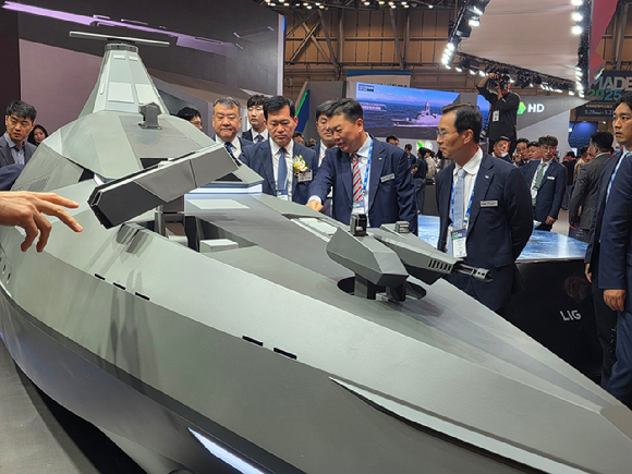 LIG넥스원이 MADEX 현장에서 미래 무인수상정의 기준이 될 콘셉트 모델 '해검-X'를 공개했다. 신익현 LIG넥스원 대표이사(오른쪽)와 석종건 방위사업청장(코사지 착용), 신용화 LIG넥스원 미래전장사업본부장이 해검-X에 관해 대화를 나누고 있다. [사진=LIG넥스원]