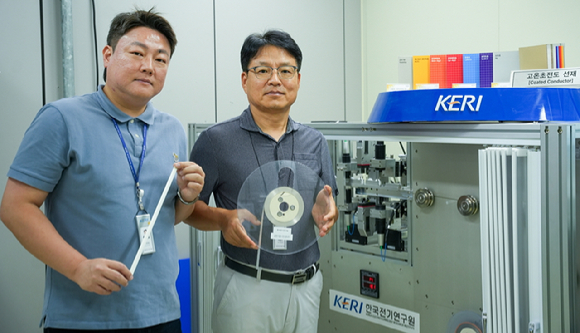 KERI 박인성&middot;하홍수 박사(왼쪽부터)가 고온초전도 선재를 들고 3D 비접촉 초정밀 검사 장비 옆에서 포즈를 취하고 있다. [사진=KERI]