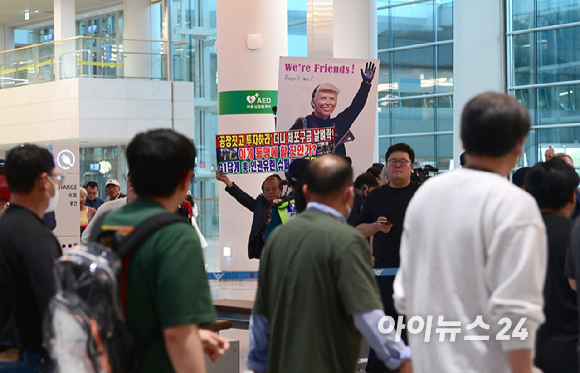 미국 이민당국에 의해 조지아주에 구금됐던 한국인 근로자들이 12일 인천국제공항 제2여객터미널 입국장을 나서며 한 시민단체가 준비한 도널드 트럼프 미국대통령 얼굴 배너를 바라보고 있다. [사진=정소희 기자]