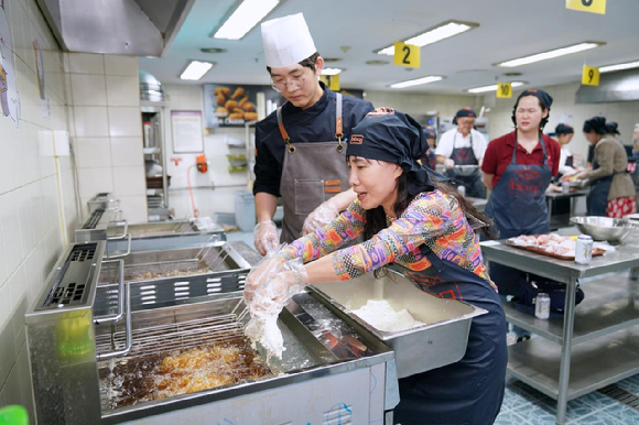 BBQ 치킨대학 치킨캠프에 참여한 태국 관광객이 튀김기에 황금올리브 치킨을 튀기고 있다. [사진=BBQ]
