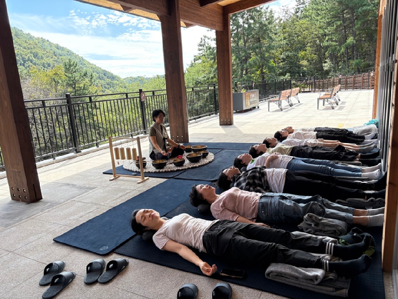 26일 국립부산승학산치유의숲에서 내맘돌봄 캠프 참가자가 싱잉볼 명상 산림치유프로그램에 참여하고 있다. [사진=한국산림복지진흥원 ]