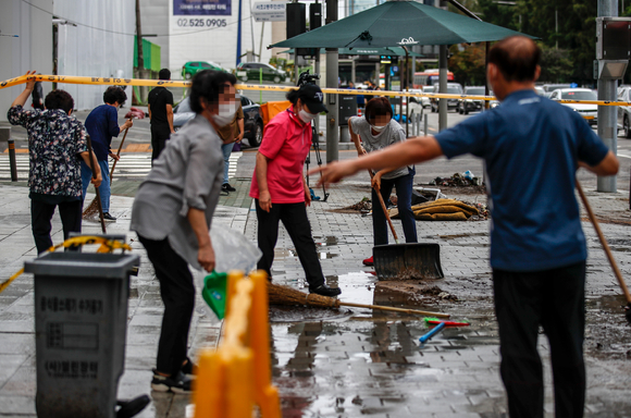 폭우가 소강 상태를 보인 지난 10일 오전 서울 서초구 서초대로 인근 빌딩에서 관계자들이 인도를 청소하고 있다. [사진=뉴시스]