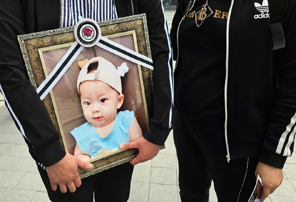  경기 화성시의 한 어린이집에서 생후 9개월 된 아이를 학대해 숨지게 한 혐의로 징역 18년을 선고받았던 어린이집 원장이 또 다른 아동학대 혐의가 드러나 추가 실형을 선고받았다. 사진은 경기 화성시의 한 어린이집 원장의 아동학대 행위로 숨진 아이의 부모가 아이의 영정사진을 들고 있는 모습. [사진=뉴시스]