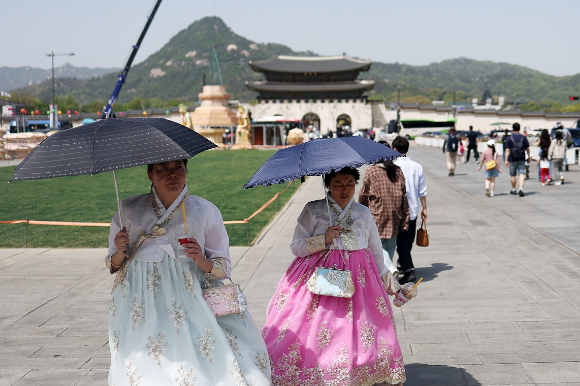 서울 광화문광장에서 한복을 입고 양산을 쓰고 걷고 있는 시민들 [사진=연합뉴스]