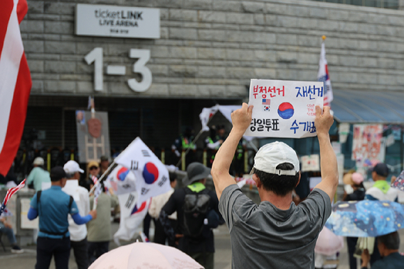 6&middot;3 지방선거 투표용지 부족 사태로 인한 '개표소 봉쇄 시위'가 계속되고 있는 18일 서울 송파구 올림픽공원 핸드볼경기장 출입문 앞에서 참가자들이 구호를 외치고 있다. 2026.6.18 [사진=연합뉴스]