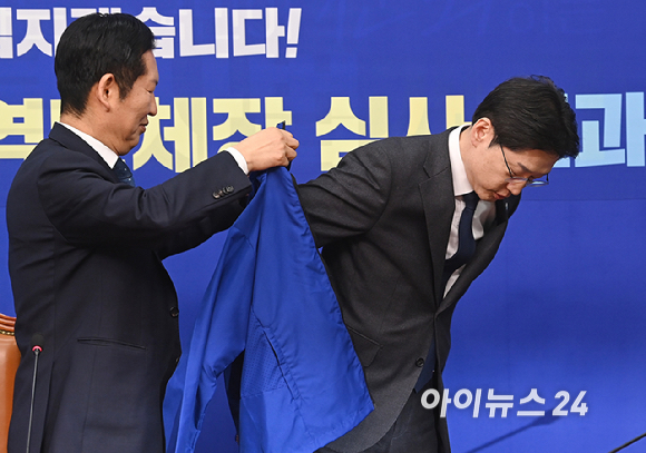 정청래 더불어민주당 대표가 5일 서울 여의도 국회에서 열린 중앙당공천관리위원회 공천 심사 발표에서 경남도지사 후보로 확정된 김경수 지방시대위원장에게 선거복을 입혀주고 있다. [사진=곽영래 기자]