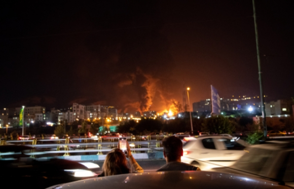 지난해 테헤란의 한 정유소가 밤사이 이스라엘의 공습을 받은 후 심한 연기와 불이 피어오르는 것으로 보고 있는 이란인들. [사진=UPI/연합뉴스]