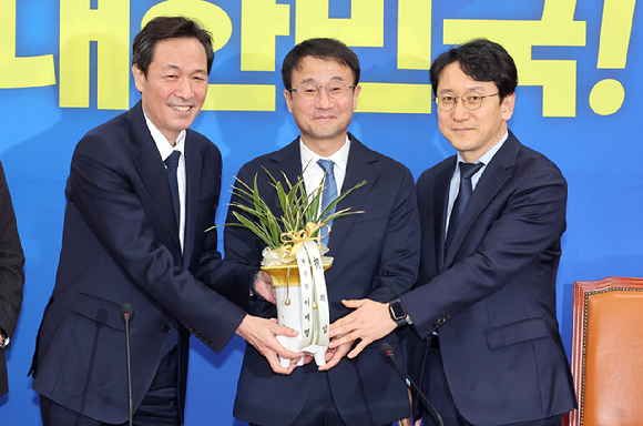 더불어민주당 한병도 신임 원내대표(가운데)가 12일 국회에서 우상호 청와대 정무수석을 만나 이재명 대통령의 축하 난을 받고 있다. 오른쪽은 천준호 신임 원내운영수석부대표. 2026.1.12 [사진=연합뉴스]