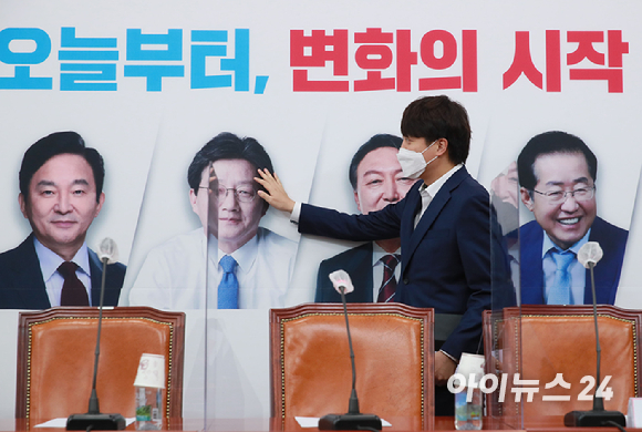 이준석 국민의힘 대표가 1일 서울 여의도 국회에서 열린 최고위원회의에 참석하며 배경판에 나온 대선 경선 후보자들의 얼굴을 살펴보고 있다.