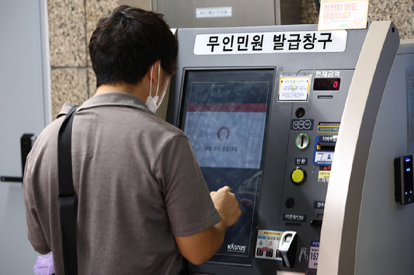 27일 서울 시내 한 지하철역에 설치된 무인민원발급기에서 한 시민이 서류가 발급되지 않아 '자료 수신 중입니다'라는 문구가 나오는 화면을 바라보고 있다. [사진=연합뉴스]