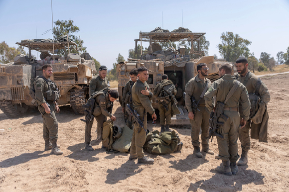 15일(현지시각) 이스라엘 남부, 가자지구 국경 인근에 주둔 중인 이스라엘 군인들이 병력수송장갑차(APC) 주변에 모여 얘기를 나누고 있다. [사진=뉴시스]