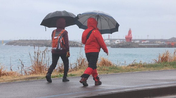 비가 오는 가운데 제주시 내도동 해안도로에서 비옷과 우산으로 무장한 올레꾼들이 걷고 있다. [사진=연합뉴스]