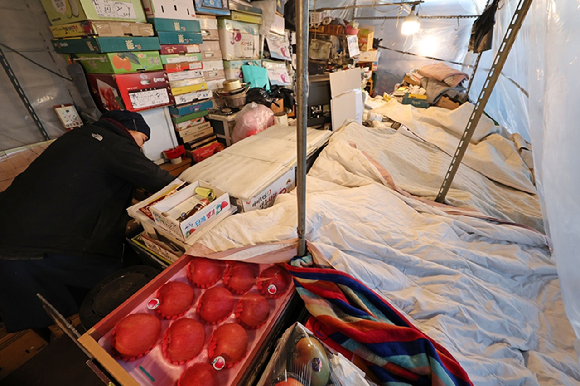 26일 한파 속 서울 송파구 가락농수산물종합도매시장의 한 점포에서 상인이 과일을 이불로 덮고 있다. [사진=연합뉴스]