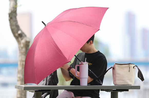 지난 23일 서울 서초구 반포한강공원에서 한 시민이 우산으로 일광을 가린 채 휴식을 취하고 있다. [사진=연합뉴스]