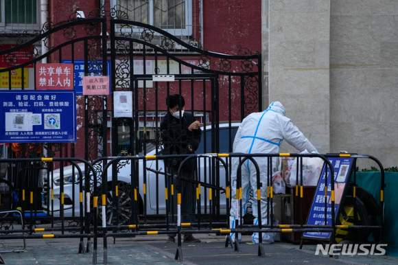 베이징의 봉쇄된 한 동네에서 마스크를 쓴 한 남성이 방역복을 입은 노동자에게 자신의 식료품을 가져가기 위해 질문하고 있다.  [사진=뉴시스]