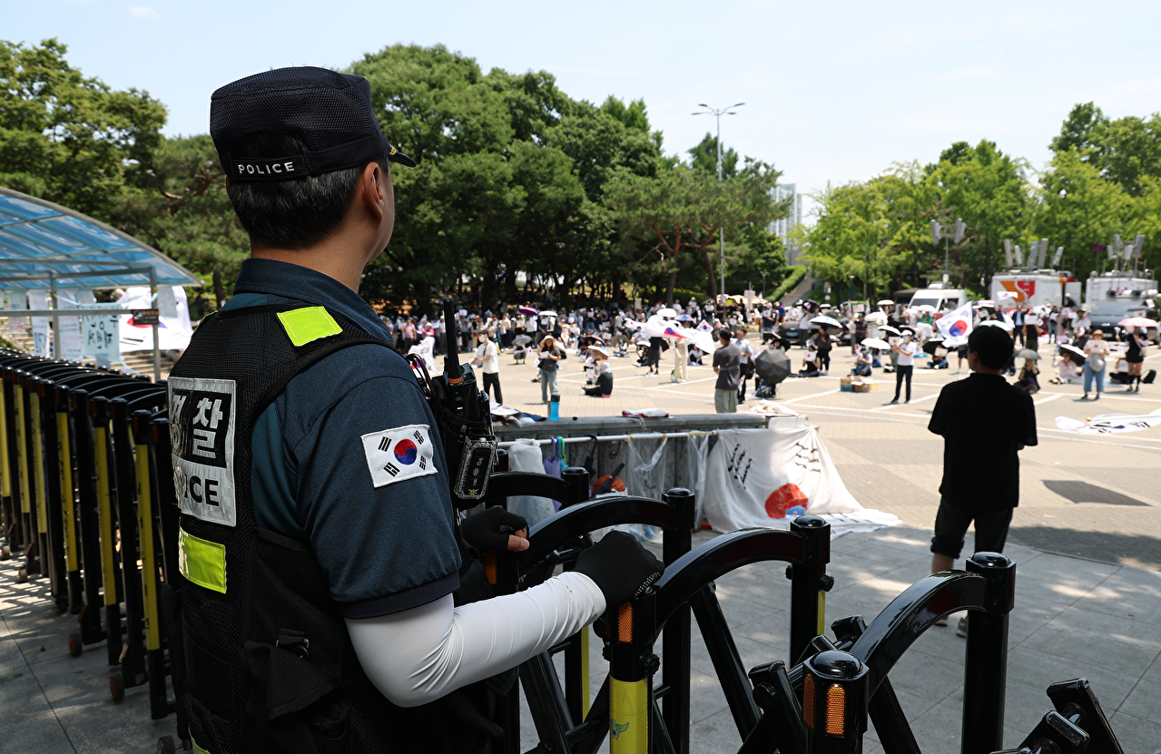 6&middot;3 지방선거 투표용지 부족 사태를 규탄하며 재선거를 요구하는 '잠실 개표소 봉쇄 시위'가 계속되고 있는 지난 9일 서울 송파구 올림픽공원 핸드볼경기장 출입구 앞에서 한 경찰이 집회를 지켜보고 있다. 2026.6.9 [사진=연합뉴스]