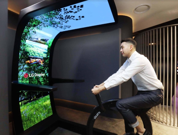 LG디스플레이 직원이 대형 OLED 스크린과 운동기구를 합친 콘셉트 제품 '버추얼 라이드'를 체험하고 있다 [사진=LG디스플레이]