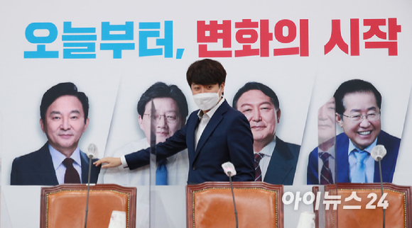 이준석 국민의힘 대표가 1일 서울 여의도 국회에서 열린 최고위원회의에 참석하며 배경판에 나온 대선 경선 후보자들의 얼굴을 살펴보고 있다.