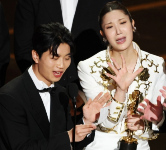 넷플릭스 애니메이션 영화 &lsquo;케이팝 데몬 헌터스&rsquo;의 주제곡 &lsquo;골든&rsquo;을 작곡한 더 블랙 레이블 소속 프로듀서 팀 아이디오(IDO)와 작곡가 24, &lsquo;골든&rsquo;을 작곡하고 직접 부른 이재(EJAE), 마크 소넨블릭이 15일(현지시간) 미 로스앤젤레스 돌비 극장에서 열린 제98회 아카데미 시상식에서 주제가상을 받은 뒤 무대 위에 올랐다. IDO의 일원인 이유한이 수상소감을 발표하는 도중 퇴장을 재촉하는 음악이 흘러나오자 이재가 당혹스런 표정으로 손짓을 하고 있다. [사진=EPA /연합뉴스]