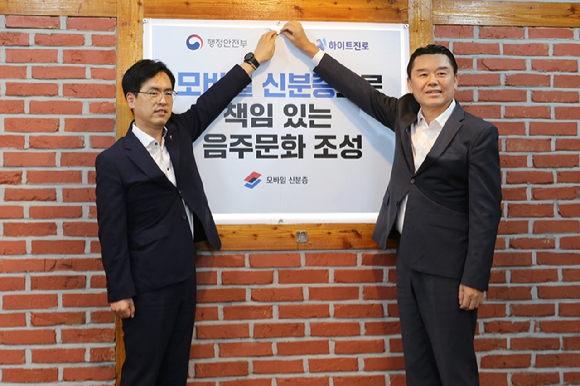 김인규 대표(왼쪽)와 김민재 행정안전부 차관이 지난 14일 행정안전부가 지정한 서울 서초동 하이트진로 본사 인근 착한가격업소를 방문해 모바일 신분증 활용을 권장하는 홍보 포스터를 부착했다. [사진=하이트진로 제공]